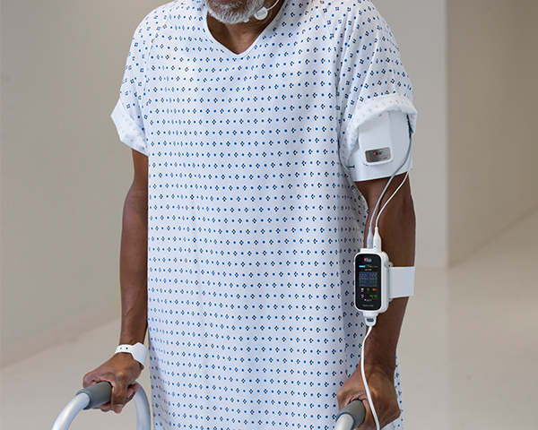 Patient walking down hospital hallway wearing gown with tetherless Radius VSM monitor connected attached to arm.