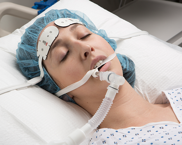 Intubated patient sleeping wearing hospital gown and surgical cap monitored by Masimo forehead sensor