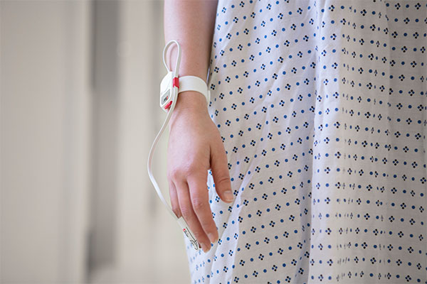 Hand of patient in hospital gown wearing Masimo sensor.